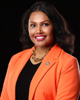 Professional headshot of a smiling woman with curly gray hair, black glasses, and a black blazer against a light background.